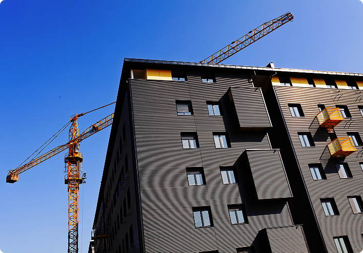 Construction crane beside a modern multi-story apartment building under development against a clear blue sky.